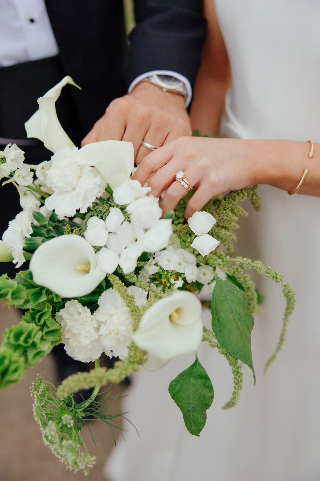 A bride and groom show their wedding rings while holding a bouquet of white flowers and greenery. for a spring wedding in Texas